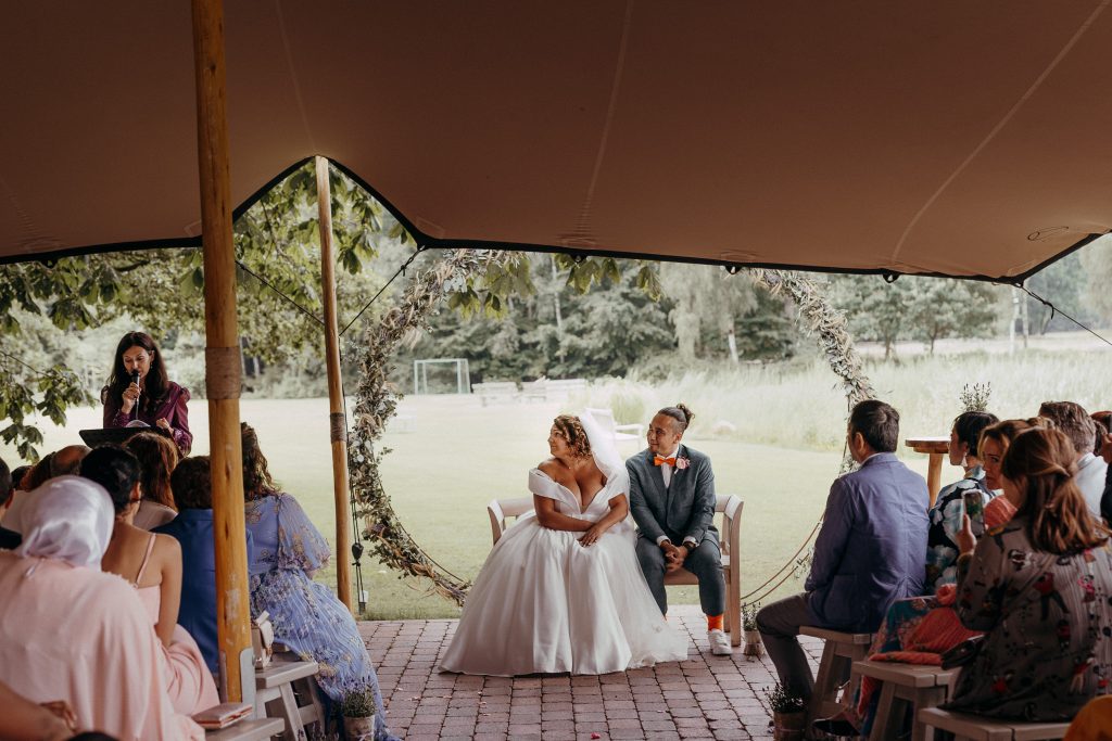 deutsch-französische freie Trauung in Norddeutschland - Hochzeitspaar sitzt unter dem Bogen, Hochzeitsgäste sitzen und Traurednerin spricht