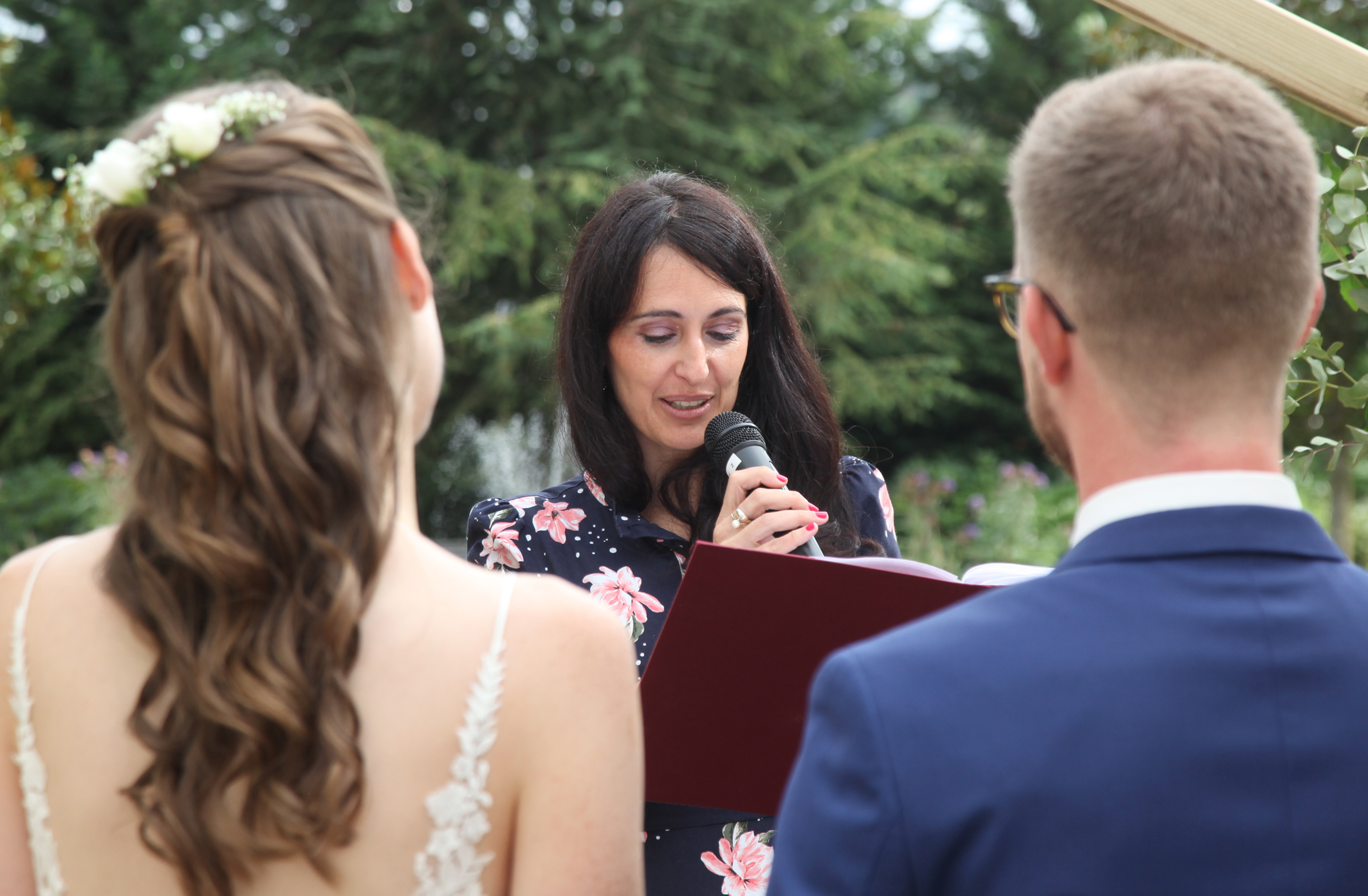 Freie Trauung eines deutsch-französischen Hochzeitspaares in der Pfalz. Traurednerin liest Ringspruch vor. Das Brautpaar steht mit dem Rücken zu den Gästen