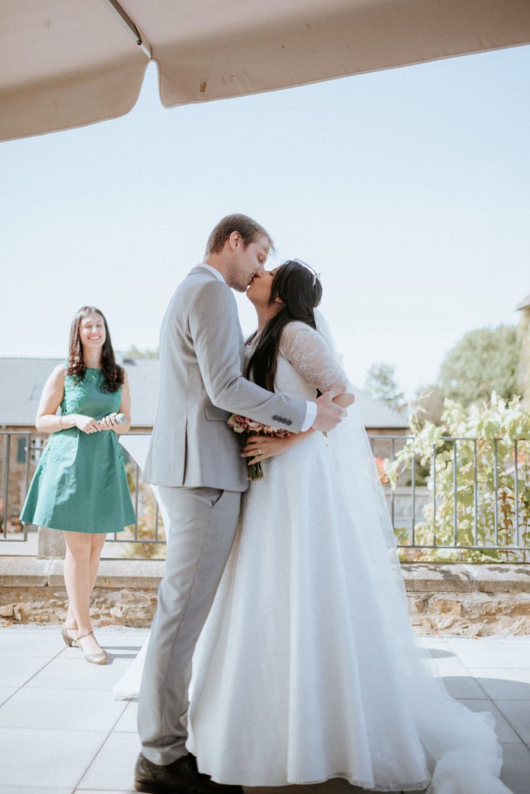 Ein sich küssendes Hochzeitspaar im Vordergrund und eine glückliche Traurednerin im Hintergrund bei dieser deutsch-spanischsprachigen freien Trauung eines deutsch-mexikanischen Paares